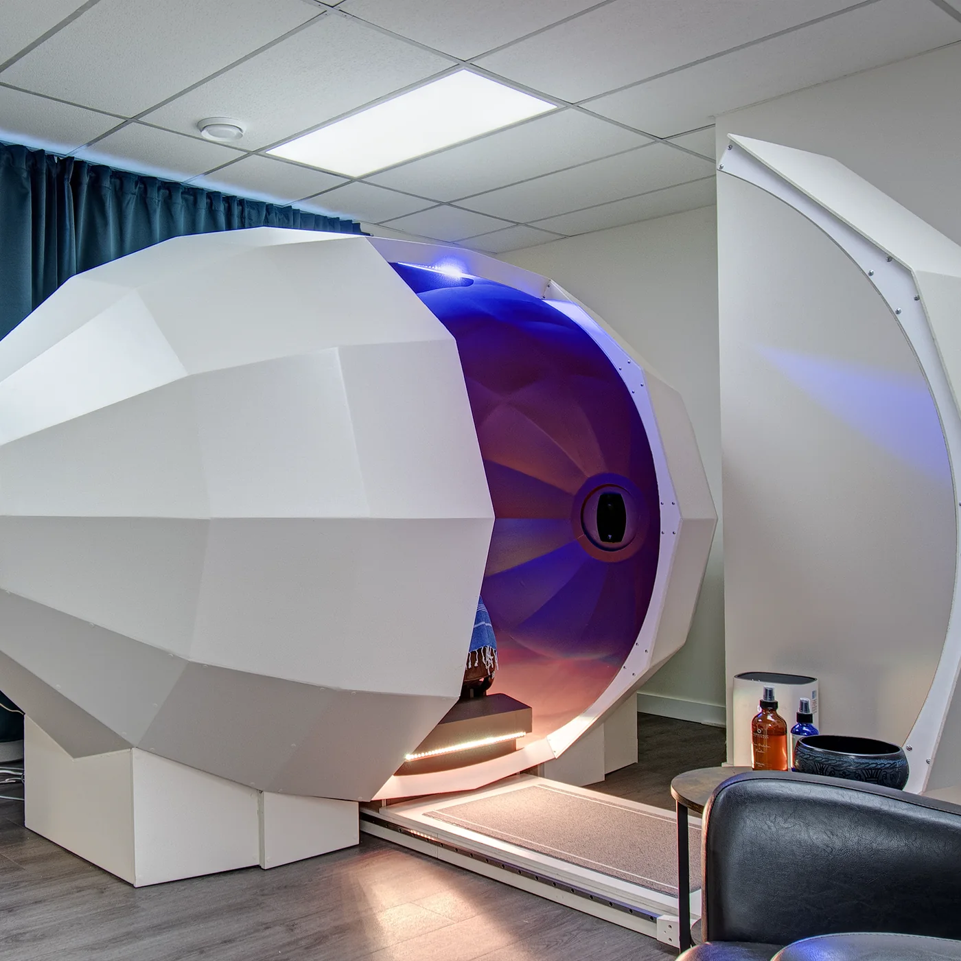 The Harmonic Egg in the treatment room, its chamber lit violet and the door open.